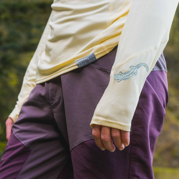 Person wearing a yellow long-sleeve sun shirt and purple pants with a blurred natural background