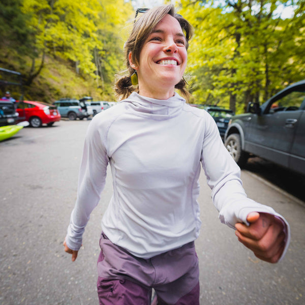 Woman in a purple long-sleeve sun shirt and purple pants standing on a road with trees in the background