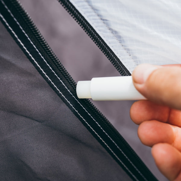Hand holding Gear Aid zipper lubricant near a zipper on a garment