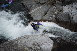 Person sliding down rock in a river launching into the water.