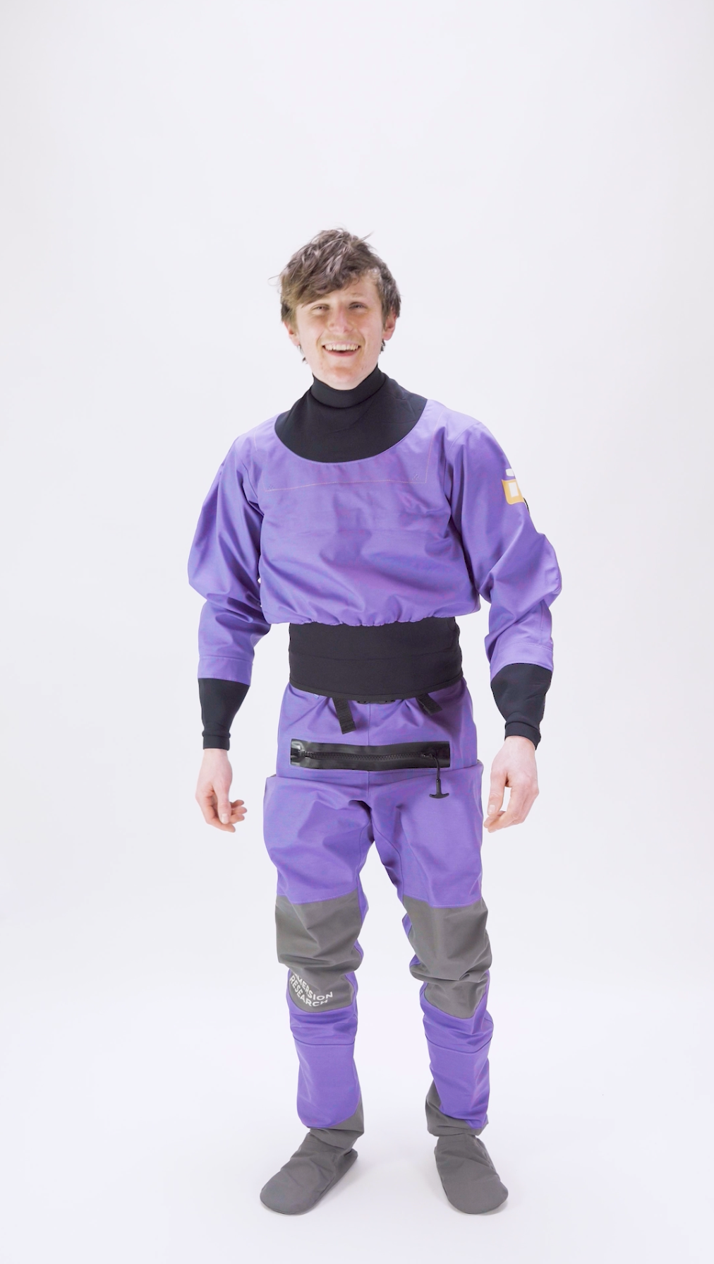 A man wearing an Immersion Research 7Figure dry suit walks into the frame and tries on the dry suit to test fit.