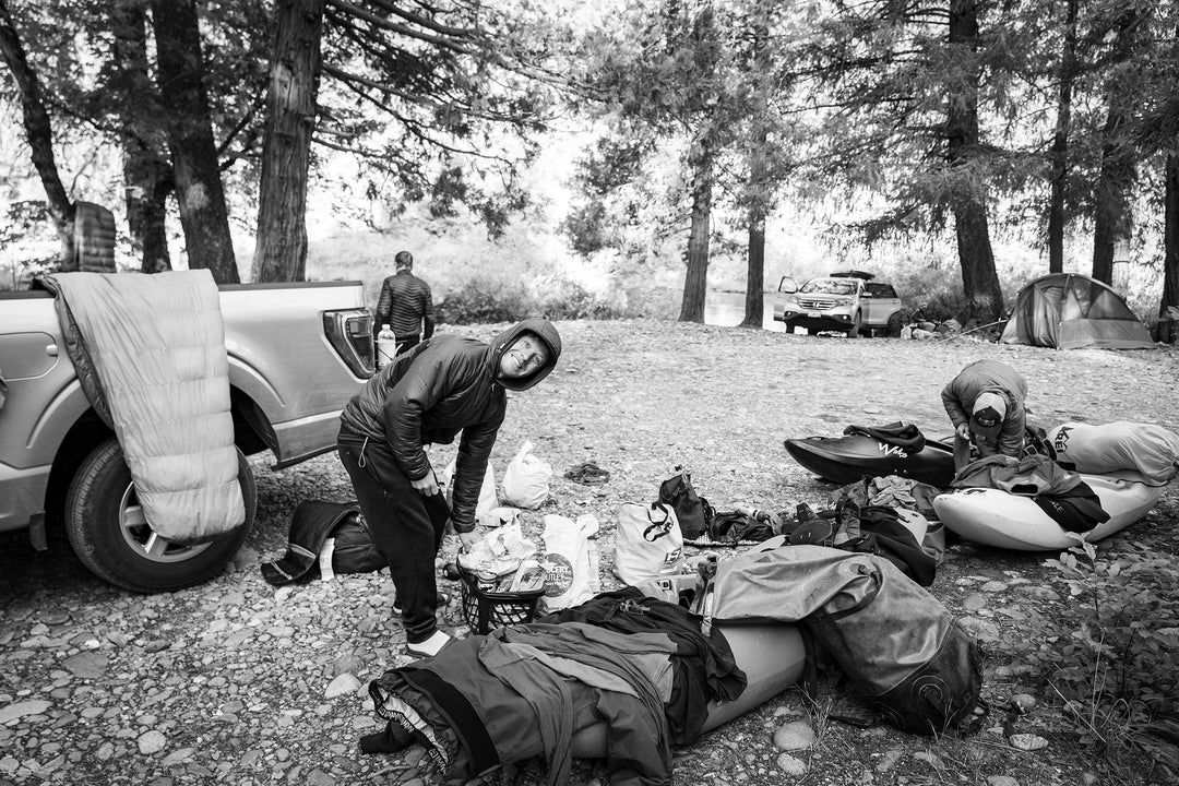 Kayaker going through gear laid out on the ground next to his pickup truck.
