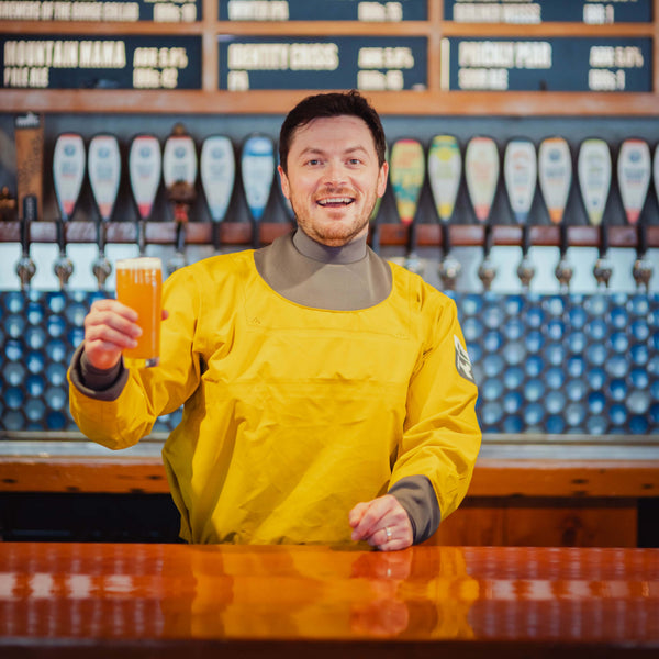Person in a yellow jacket holding a beer at a bar with beer taps in the background