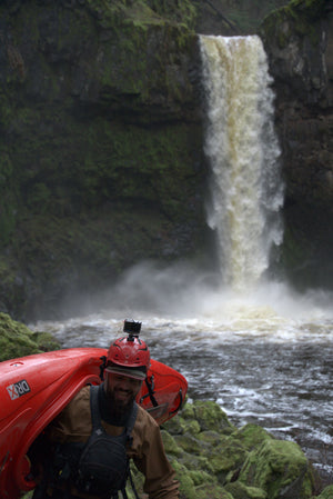 Person with a red helmet and kayak near a waterfall