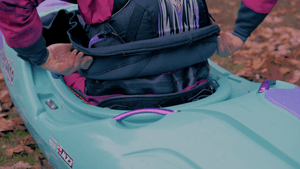 Person adjusting spray skirt in a teal kayak wearing Aphrodite Dry Suit.
