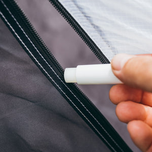 Hand holding Gear Aid zipper lubricant near a zipper on a garment