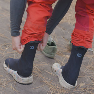 Kayaker putting neoprene socks on over dry suit booties