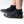 A person wearing black neoprene boot covers with black rubber soles, shown from the calves down on a clean white studio background. A gray IR logo.