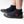 A person wearing black neoprene boot covers with black rubber soles, shown from the calves down on a clean white studio background. A red IR logo.