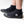 A person wearing black neoprene boot covers with black rubber soles, shown from the calves down on a clean white studio background. A white IR logo.