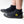 A person wearing black neoprene boot covers with black rubber soles, shown from the calves down on a clean white studio background. A yellow IR logo.