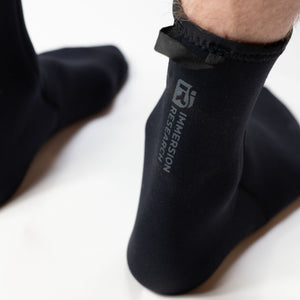 Black neoprene socks with 'Immersion Research' logo worn by a person on a white background