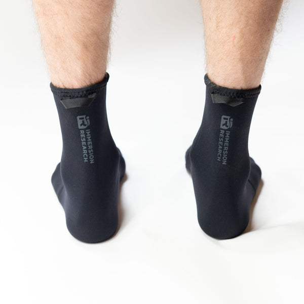 Black neoprene socks with 'Immersive Research' logo on backside of sock worn by a person on a white background