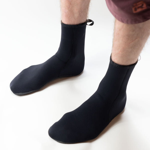 Black neoprene socks worn on feet against a white background