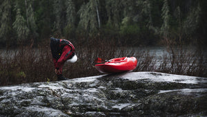 Whitewater kayaker in an immersion research dry suit stretching by the river.