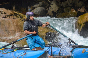 Raft guide rowing down the river in an Immersion Research paddle jacket.