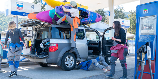 A group of kayakers at a gas station loading up a car to go kayaking.