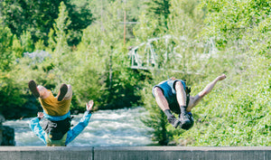 A guy and a girl doing a backflip off a bridge into the river.