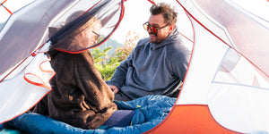 A woman and man sitting in a tent wearing hot lap hoodies by Immersion Research.