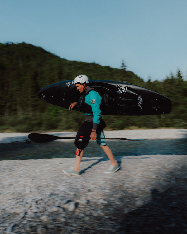 Person carrying a paddleboard on a beach with trees in the background