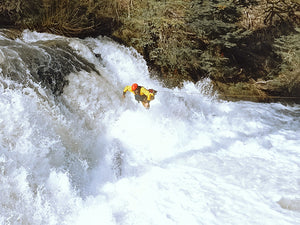 A man wearing an Immersion Research dry suit jumping into a river rapid.