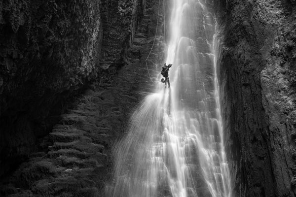 A search and rescue personnel rappelling down a canyon in an immersion research dry suit.