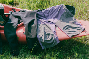 A pair of neoprene pants and shorts drying in the sun on a kayak in a grass field.