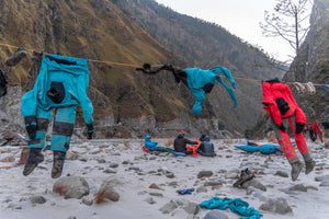 Kayakers at camp along side a river warming up by the fire as gear is hanging up to dry.
