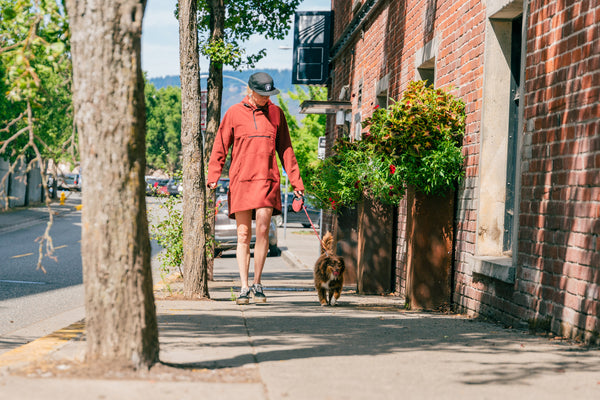 A woman walking her dog downtown in a Wind Pro Long Anorak by Immersion Research.