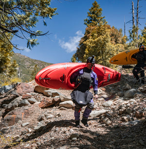 A man wearing an Immersion Research dry suit and spray skirt, hiking with his kayak.