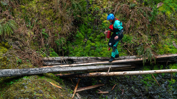 Kayaker walking across logs that have formed a bridge over a river. 