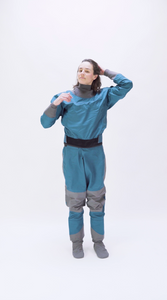 A women walks into the frame and tries on an Aphrodite dry suit by Immersion Research to see how it fits.